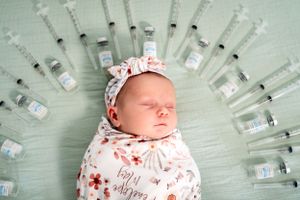 Newborn baby sleeping peacefully surrounded by arranged fertility treatment medication vials.