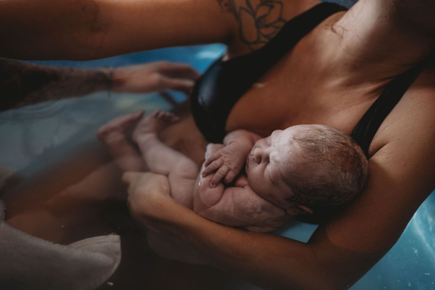 Newborn baby rests peacefully on caregiver's chest in intimate black and white photograph.