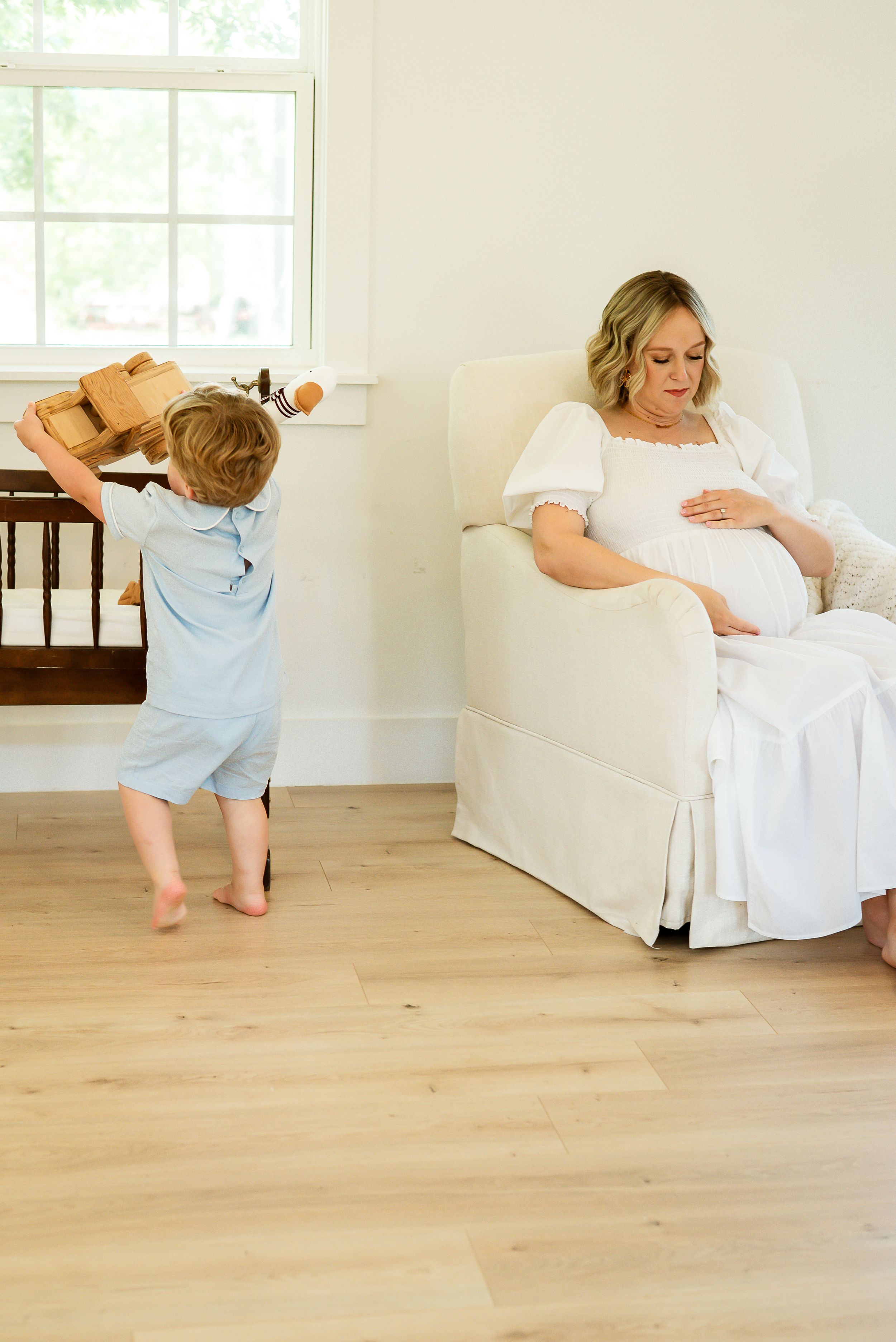 Pregnancy photo session featuring candid moment with toddler playing in bright home interior. Maternity session