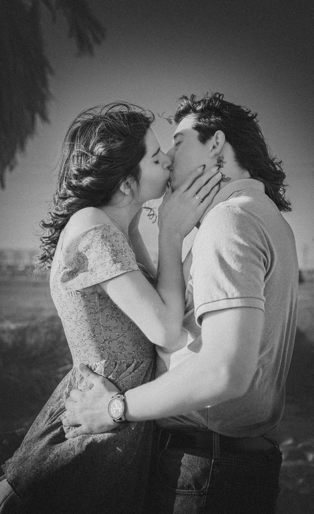 A romantic black and white photograph of a passionate kiss between two people outdoors.
