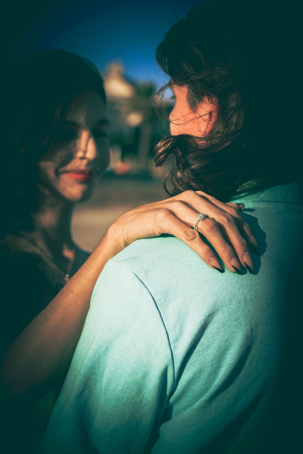 An intimate couple in dim lighting with one person wearing a light blue shirt while their hair flows in dramatic shadows.