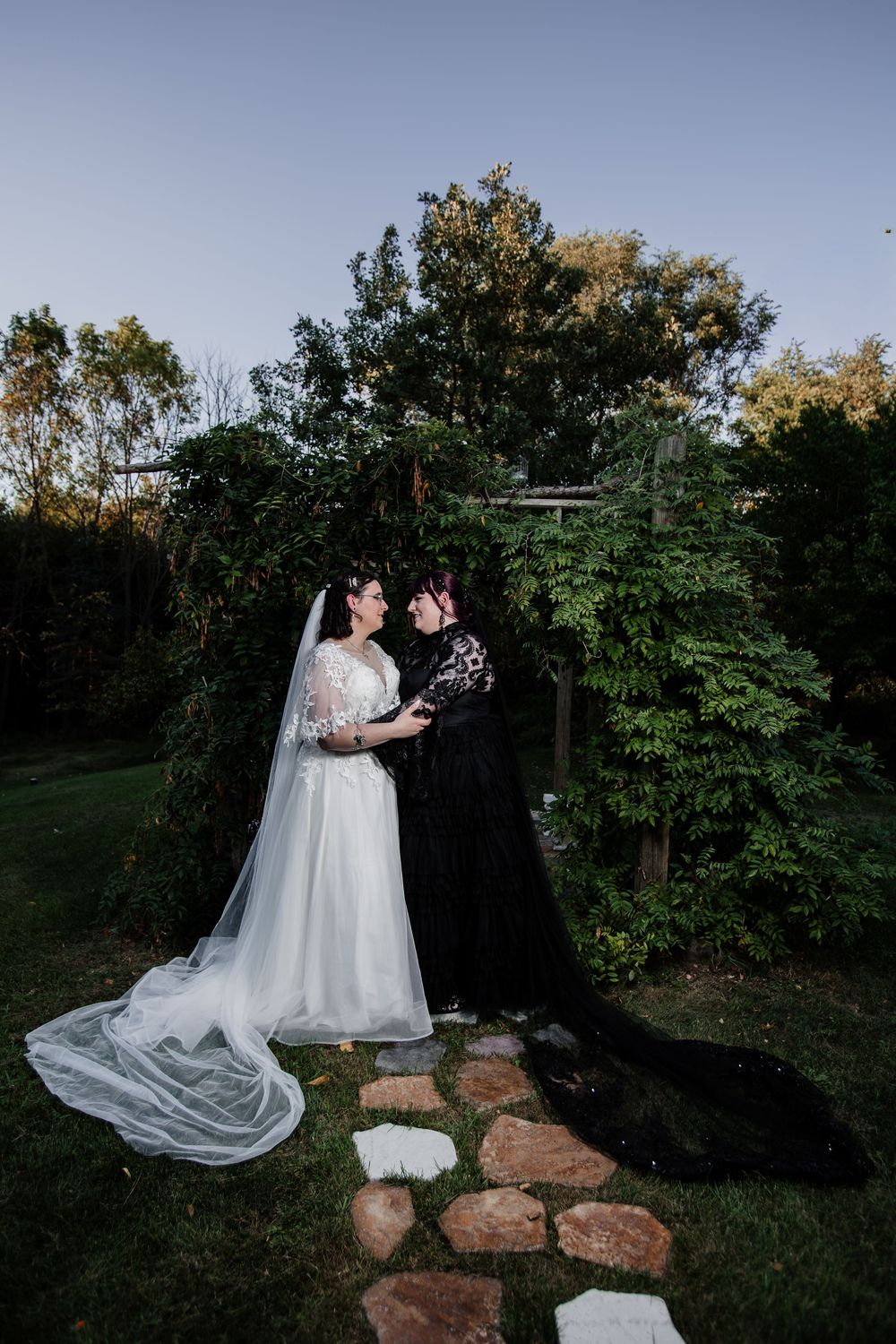 A couple in wedding attire poses on rocks in an outdoor garden setting at dusk.