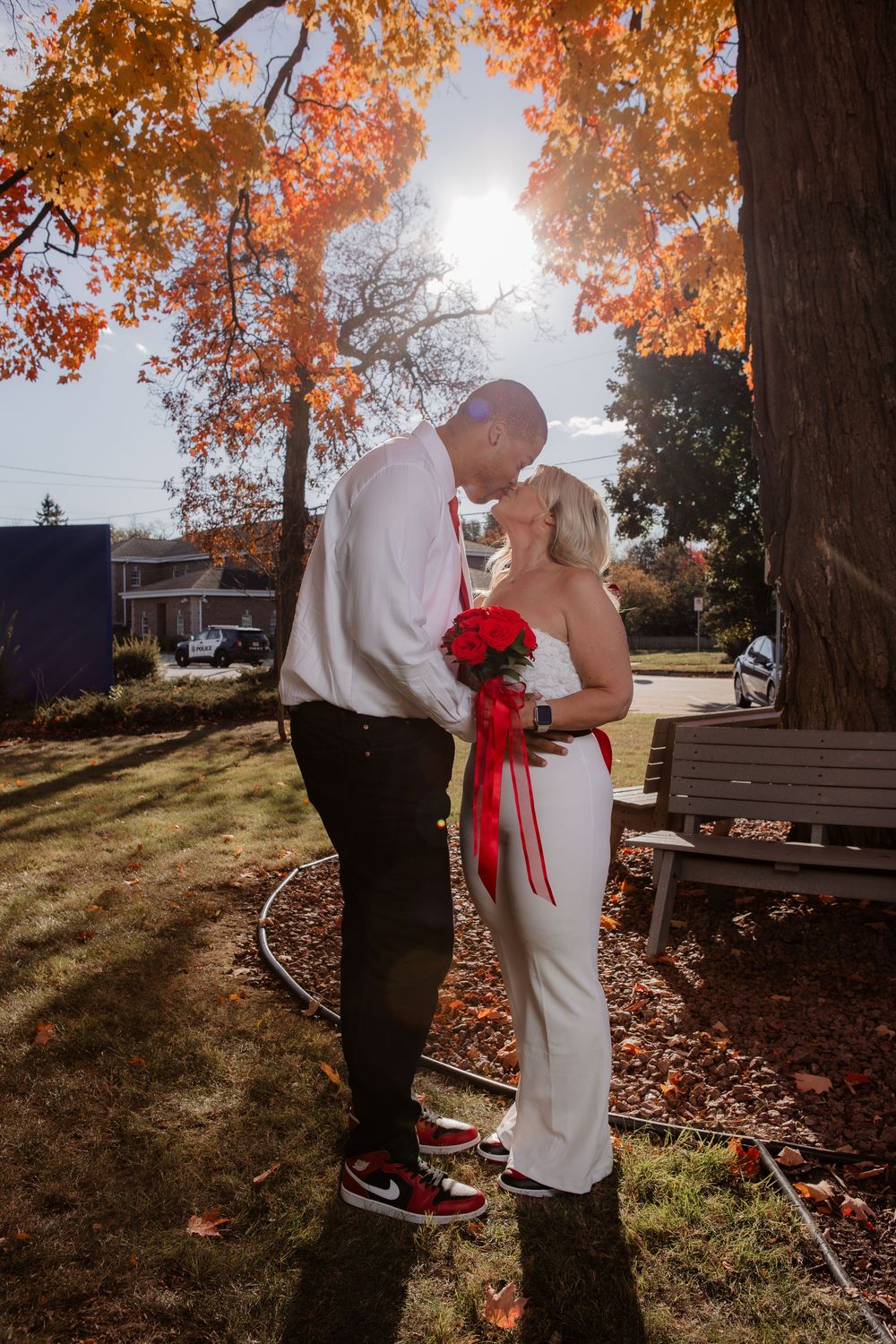 Couple embraces under autumn trees with golden leaves and sunlight streaming through the branches.