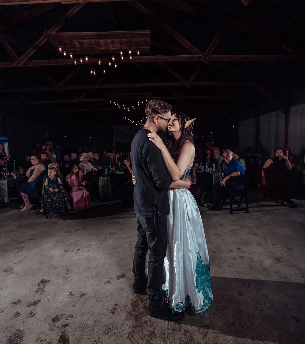 A couple shares an intimate dance moment under string lights in an indoor venue.