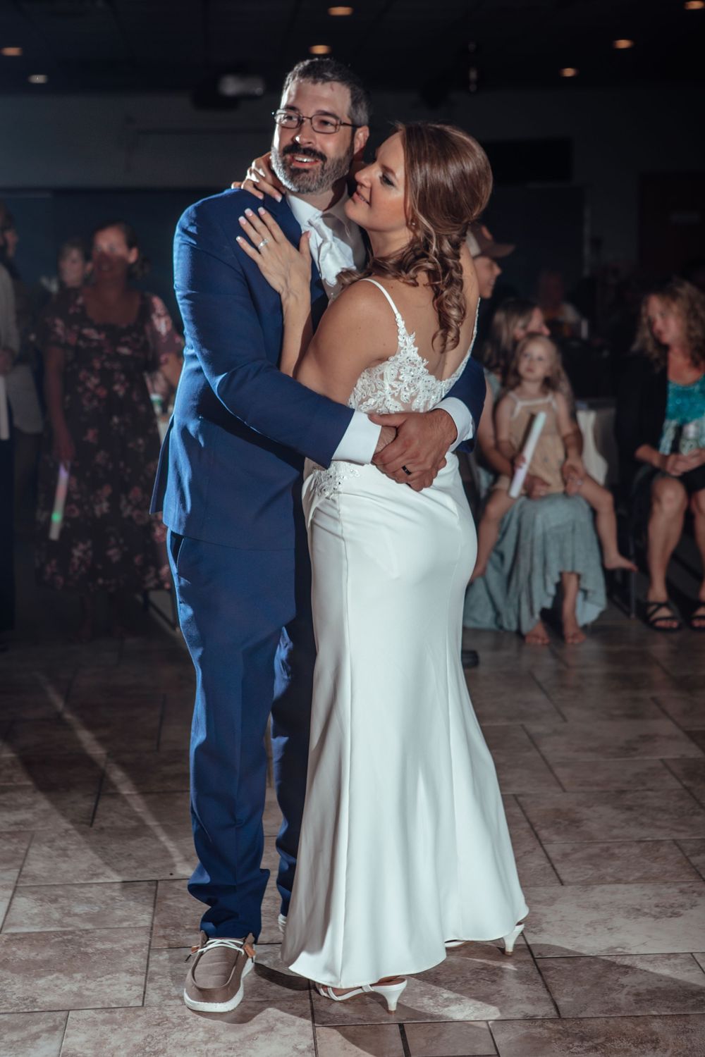 A couple shares a romantic dance together at their wedding reception on a dimly lit dance floor.