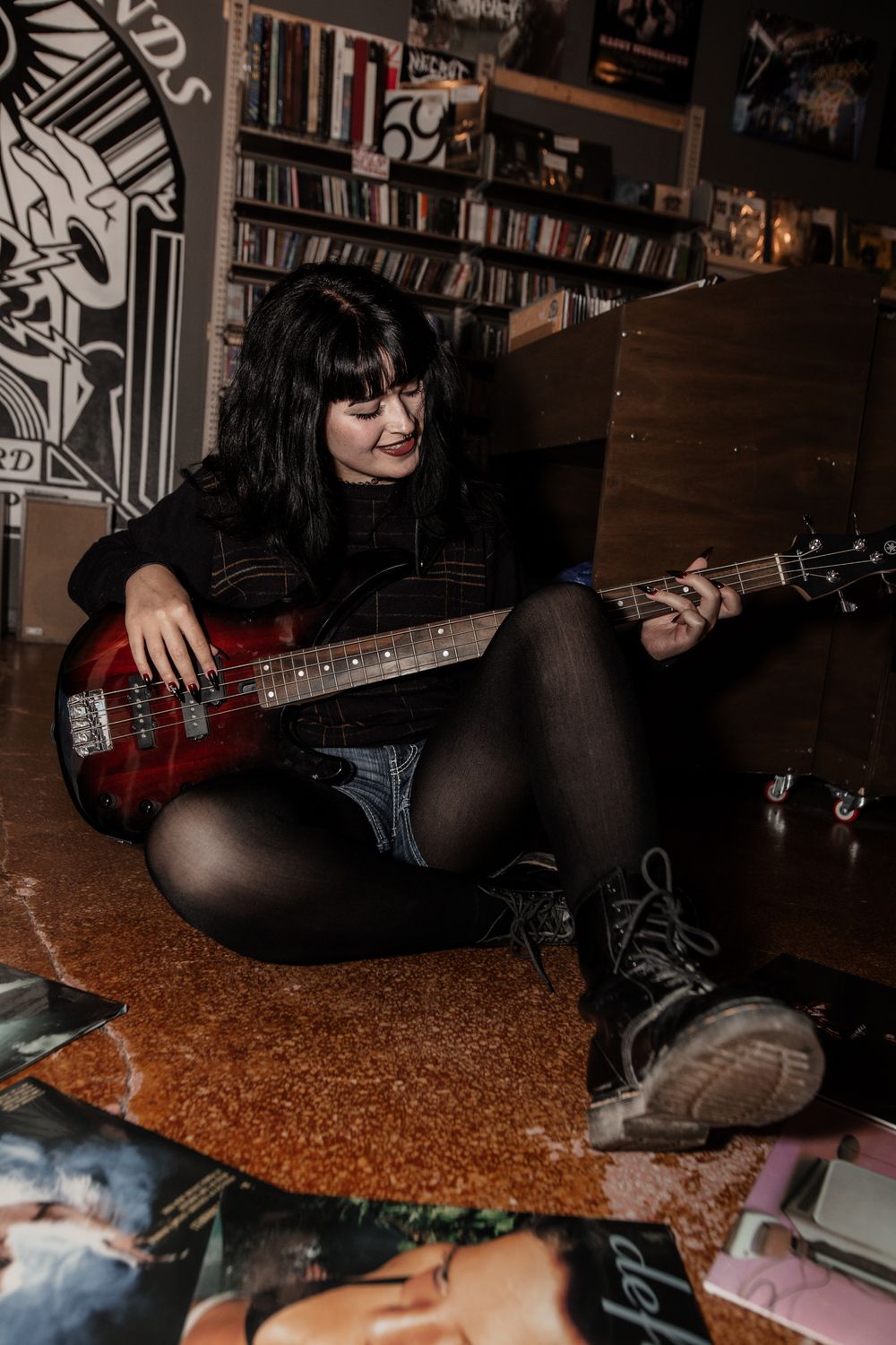 Dark moody senior photo with bass guitar and vinyl records on orange carpet.
