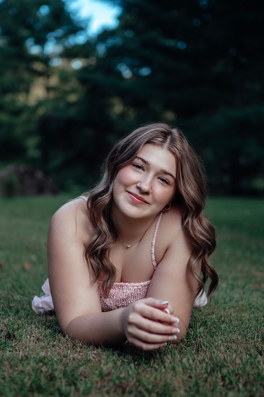Artistic senior portrait of someone lying on grass in a pink summer dress.