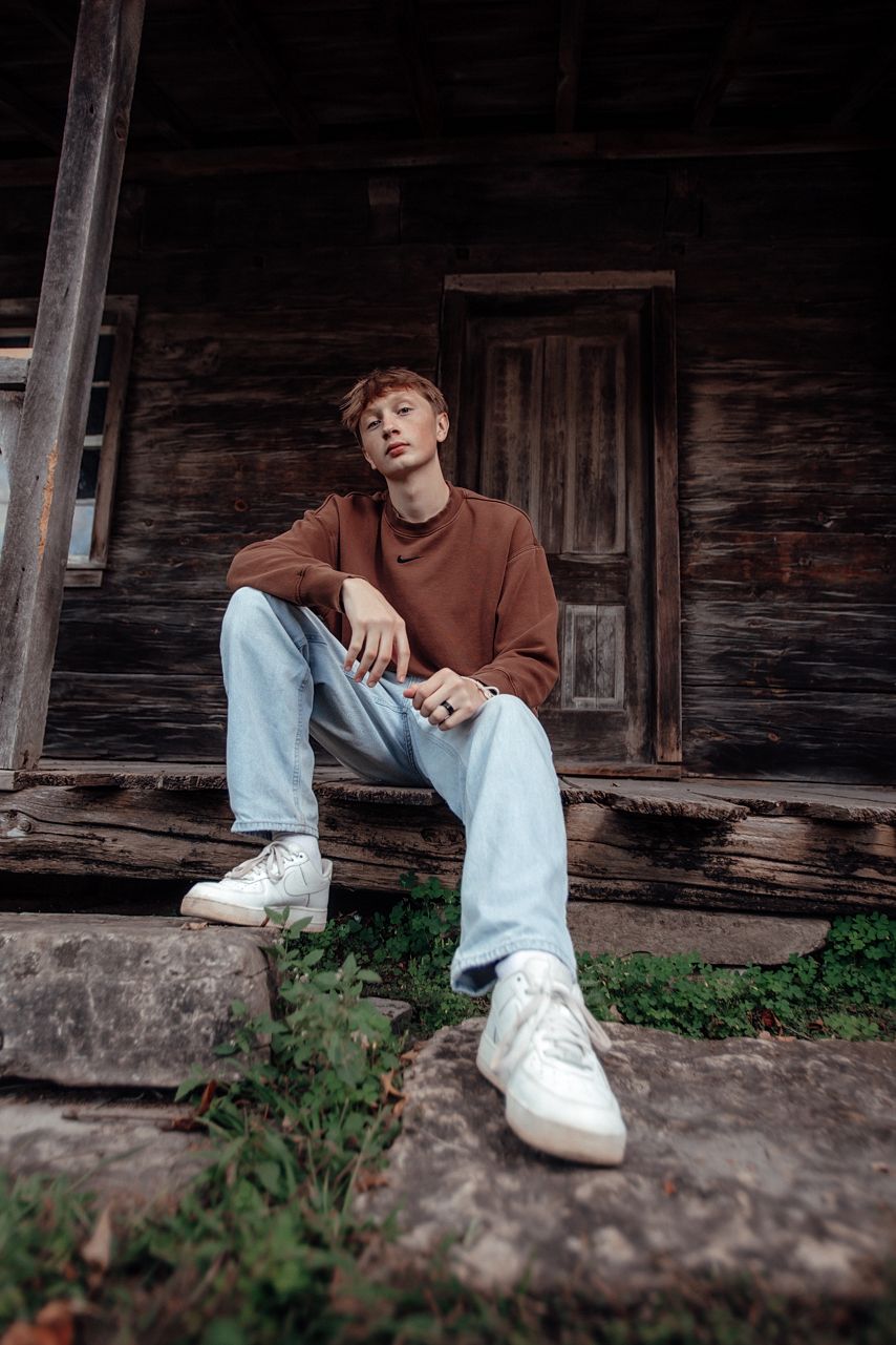 Casual senior portrait sitting on stone steps of rustic wooden cabin.