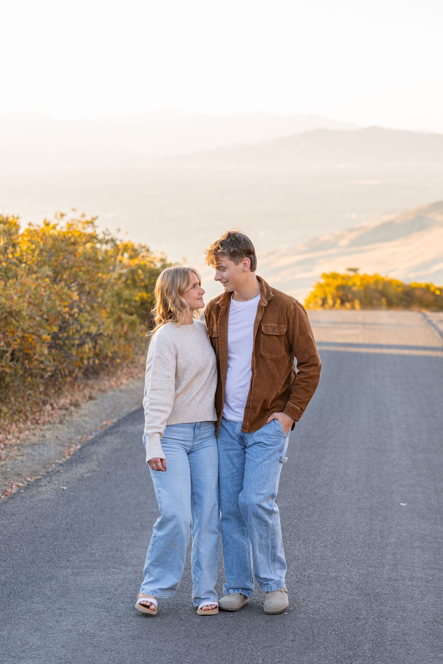 Couple in casual denim and sweaters walking together on mountain road at sunset.
