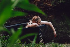 Woman laying on a boat, dangling her hand in the water with a grassy landscape behind her