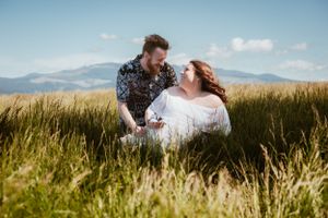 Maternity session with expecting parents at the base of a green-capped mountain in golden sunlight