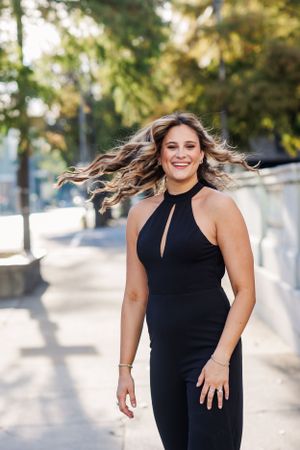 A woman in a black jumpsuit twirls with joy as her hair flows in the sunlight.