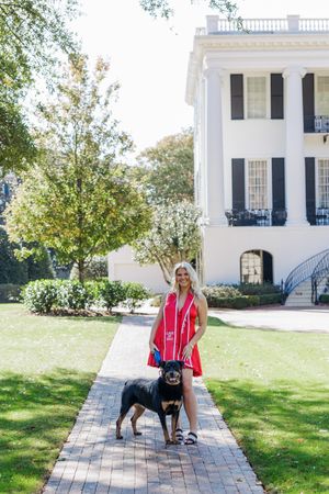 Graduate in red poses with black dog in front of white columned historic building at University of Alabama.