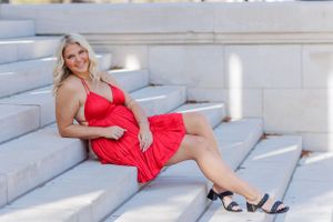 Graduate in red dress lounges on concrete stairs during glamorous photo session at University of Alabama.