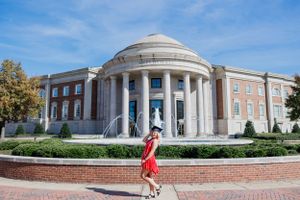 Red graduation dress contrasts against classical domed university building with white columns.