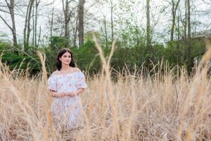 Person in white dress stands among tall golden grass with trees in background.
