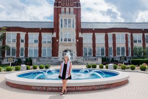 Graduation photo in front of a brick university building with a central tower and decorative fountain in the foreground.