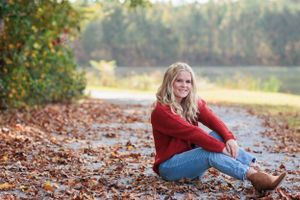 Autumn senior portrait session on path covered with fallen leaves.