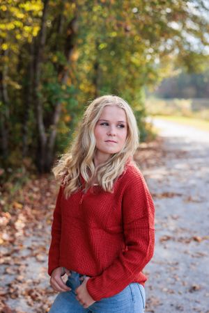 Fall fashion senior portrait on leaf-covered path with warm autumn colors.