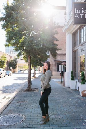 Stylish person posing on cobblestone sidewalk outside urban storefront in sunlight.