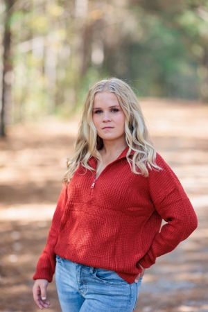 Casual outdoor senior portrait featuring red sweater against wooded background.