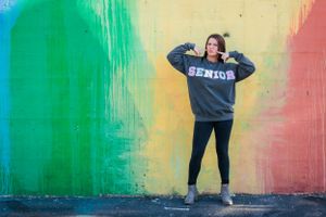 Person wearing 'GENIUS' sweatshirt poses playfully against colorful gradient wall.