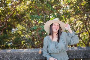 Person in sun hat and flowy top posing outdoors with natural foliage background.