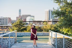 Person in burgundy dress standing on urban bridge with city skyline view.