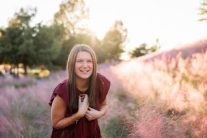 Person in burgundy dress standing in field of pink flowers during golden hour.