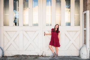 Person in red dress posing against large white barn doors.