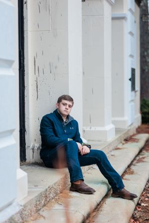 Casual portrait of person in blue jacket sitting on white building steps.