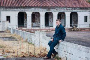 Person in navy suit sitting on stone wall next to abandoned arched building.