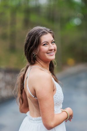 A candid outdoor portrait showing a joyful expression in a white formal dress.