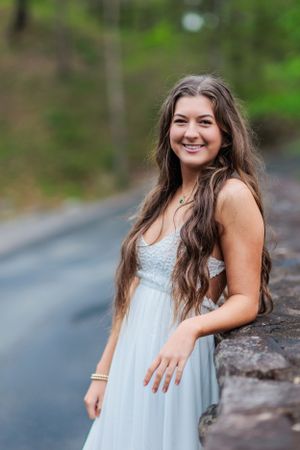 A person wearing a flowing white dress poses along a mountain road.