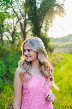 A sunlit portrait in a pink dress against a backdrop of lush green foliage.