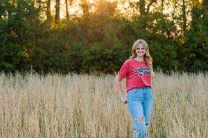 Person stands in golden field during sunset wearing red t-shirt and blue jeans.