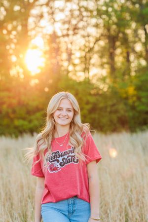 Person in red graphic tee poses in tall grass field at golden hour.