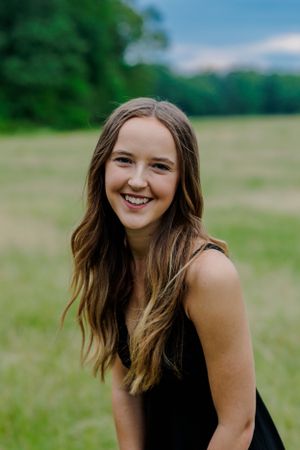 Portrait in grassy field with natural lighting and trees in background.