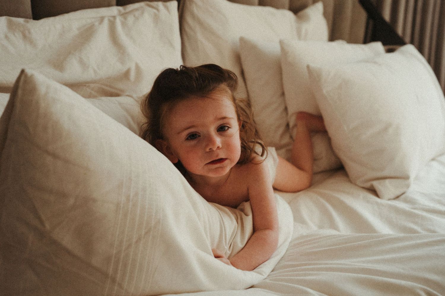 Young child smiling while nestled in crisp white bedding.