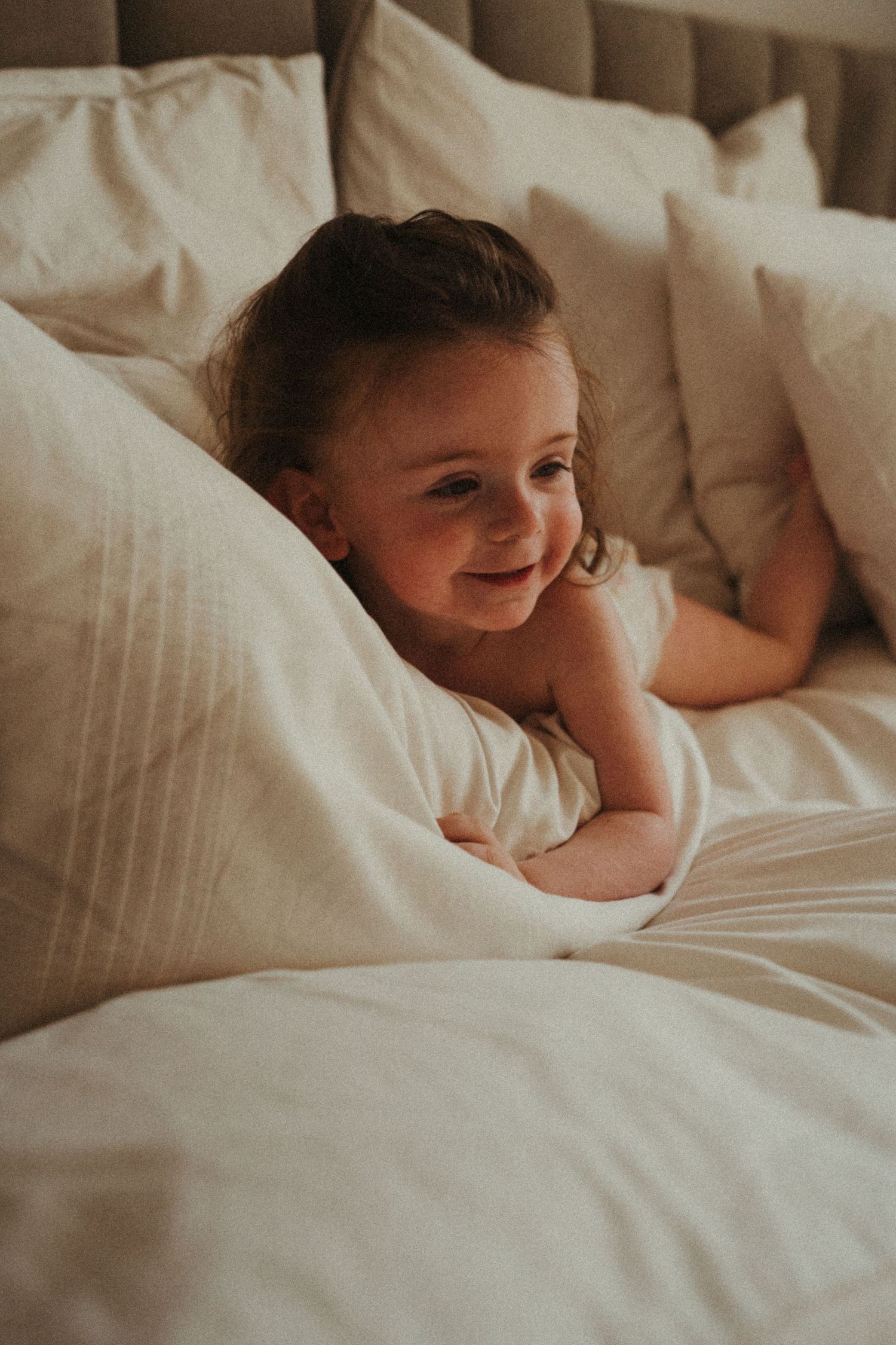 Child lying in bed with white linens showing playful expression.