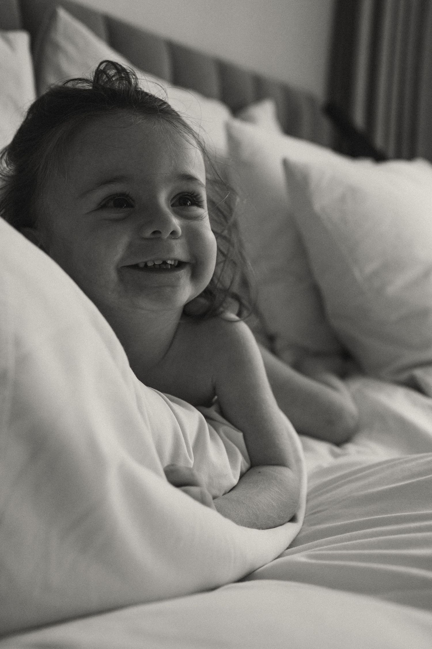 Close-up of joyful laughter while resting in bed with white linens.