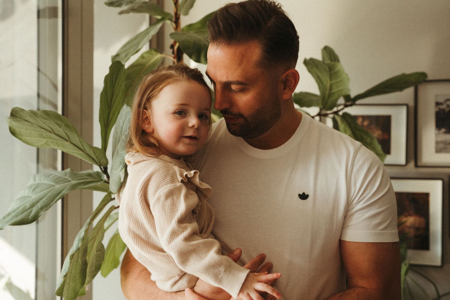 Tender moment between parent and child with a houseplant in soft natural lighting.
