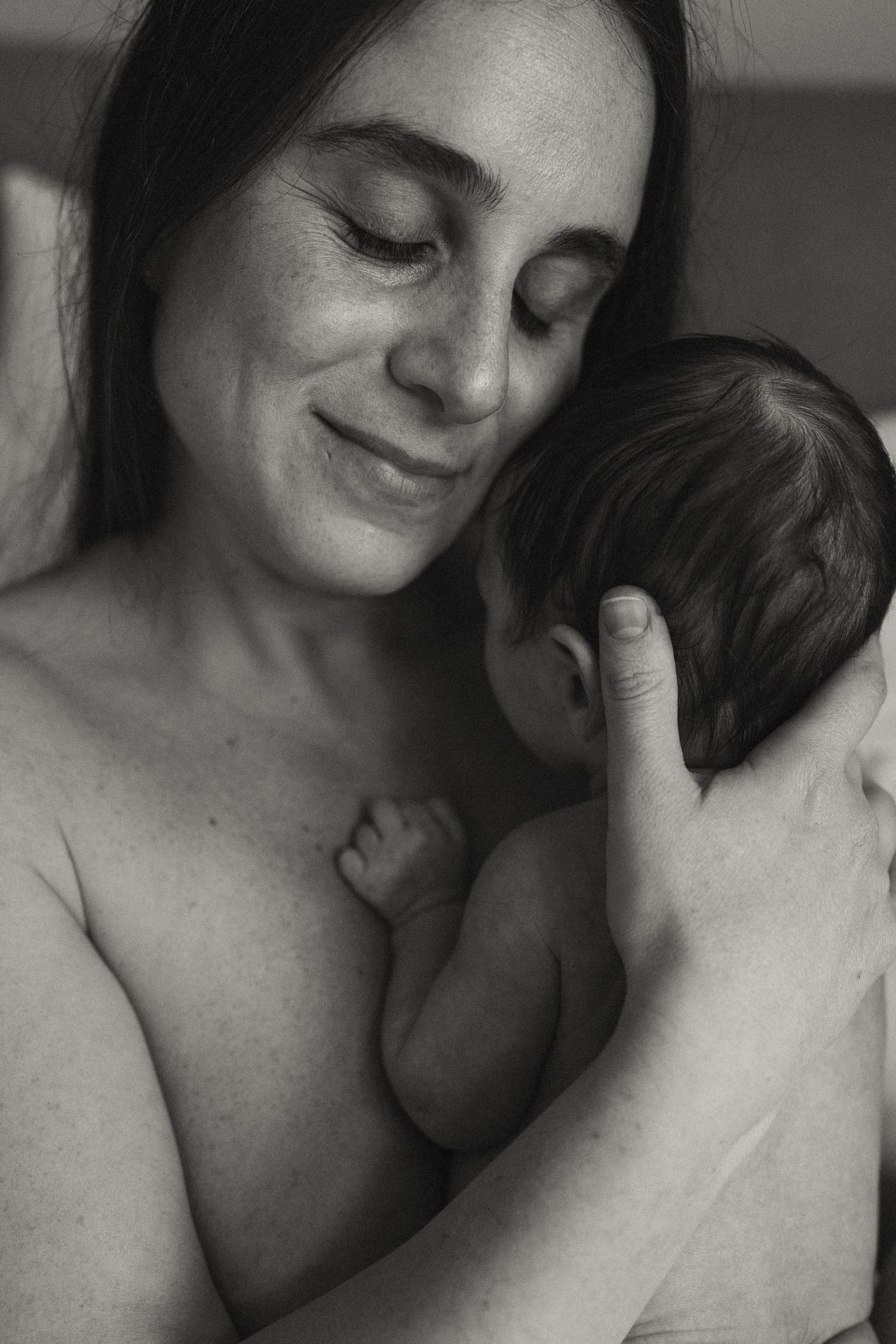 Intimate black and white portrait showing tender moment between parent and infant in natural light.