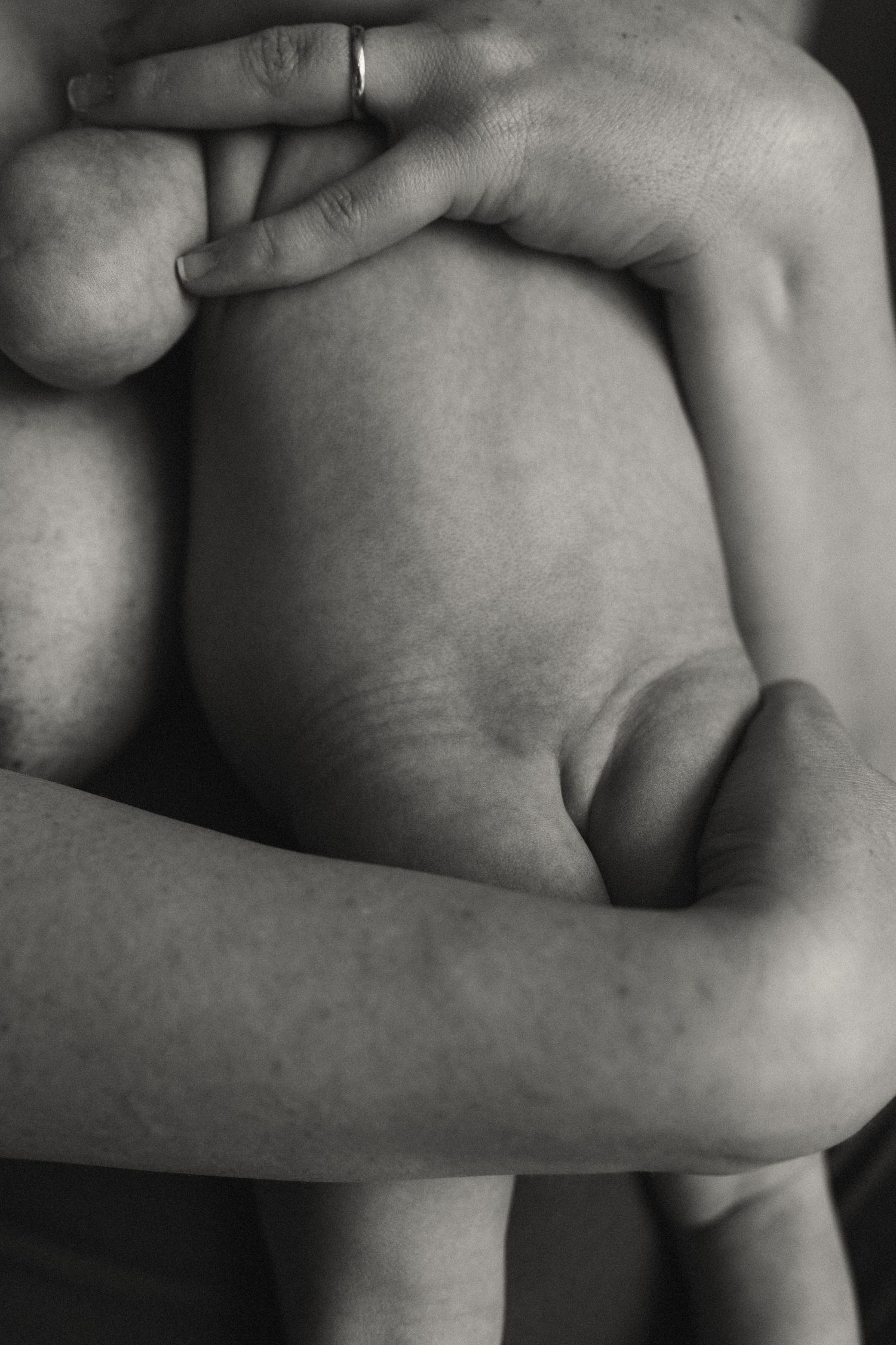 Close-up black and white detail of hands tenderly holding baby.
