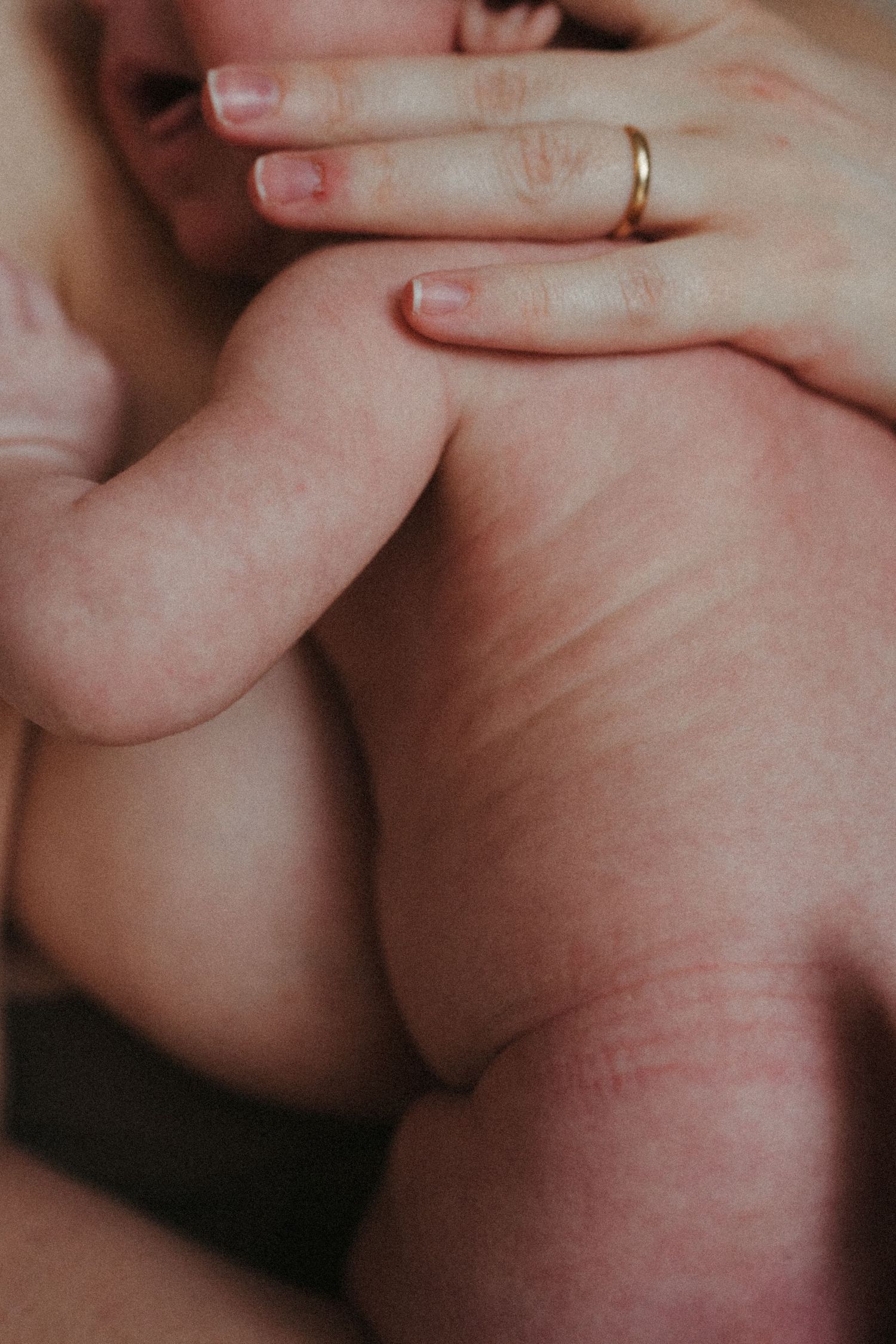 Close-up detail shot showing gentle touch and wedding ring with baby.