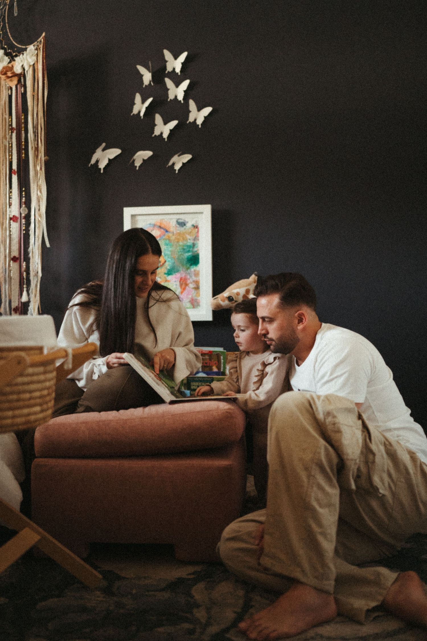 Family relaxing together on brown couch with white butterfly decorations on dark wall.