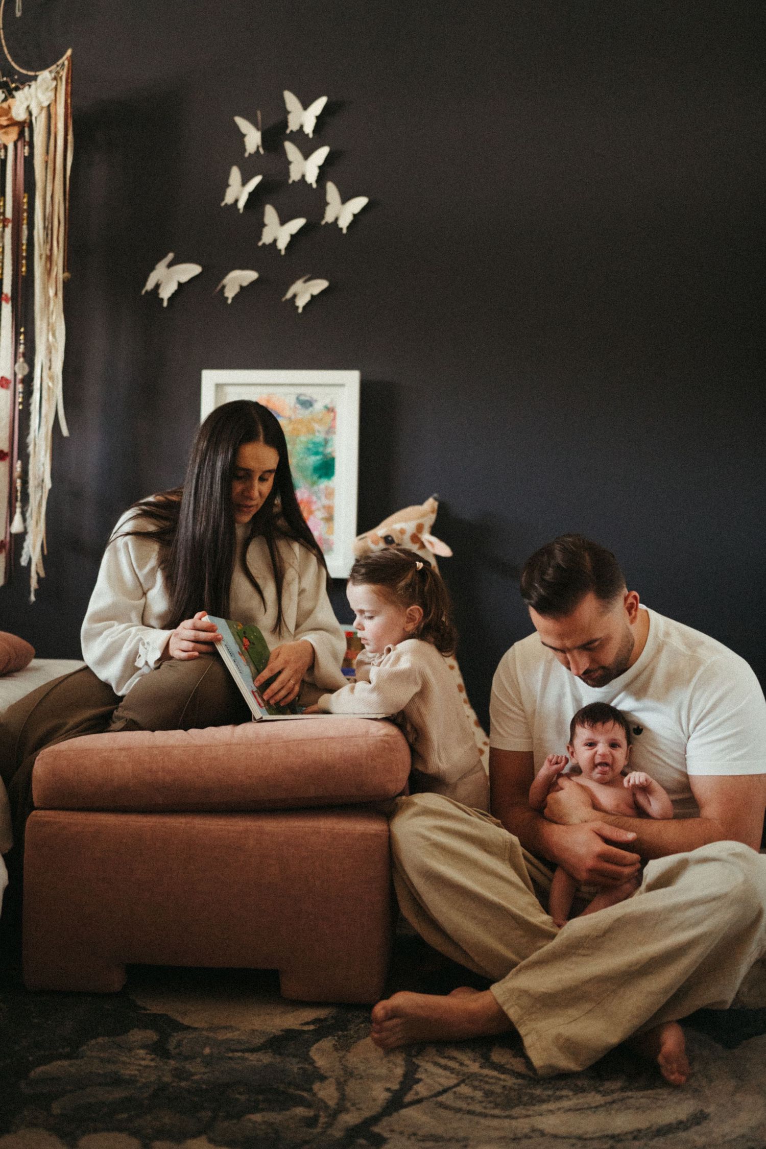 Candid family moment on couch with butterfly wall decor and warm lighting.