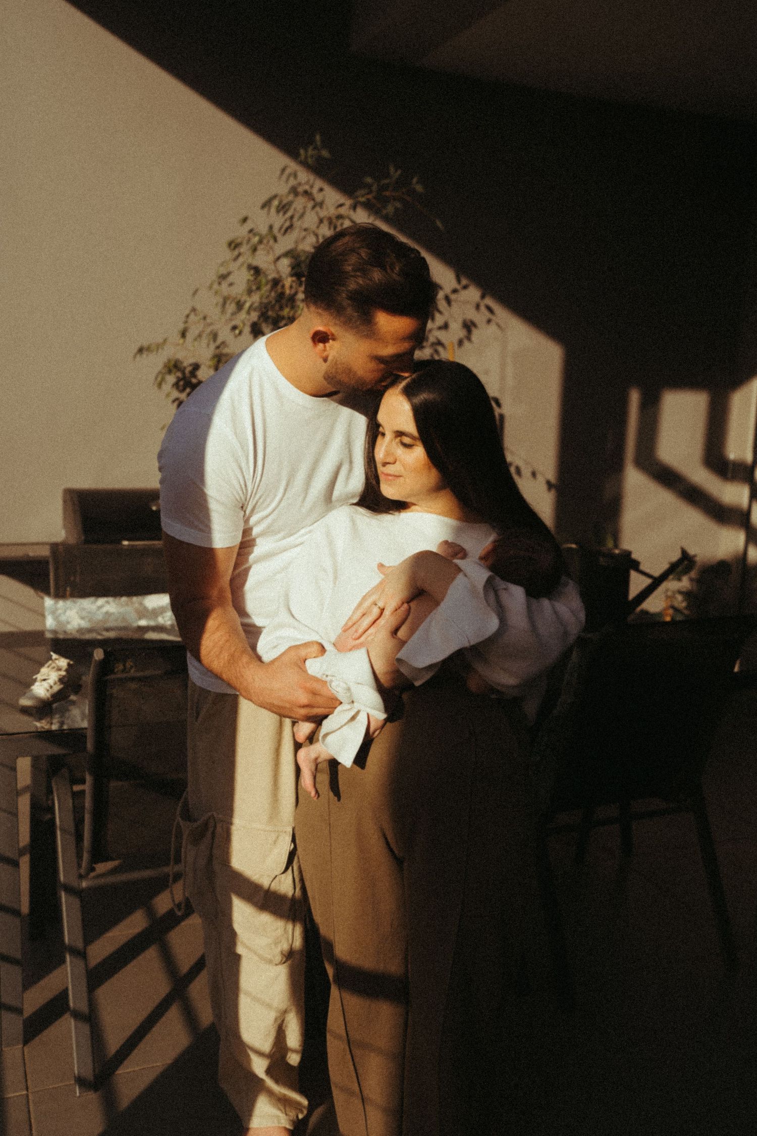 Tender moments between couple captured in natural window light and shadows.