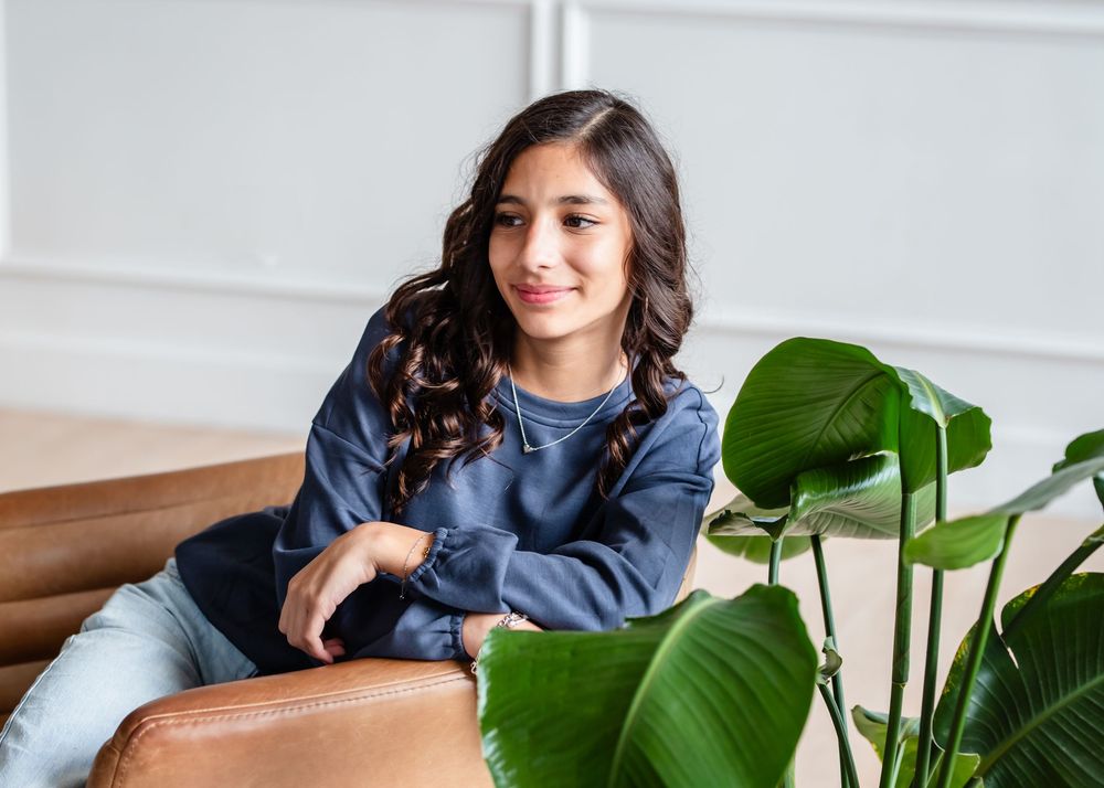 A girl sits on modern studio chair next to large green monstera plant in Houston, Texas.