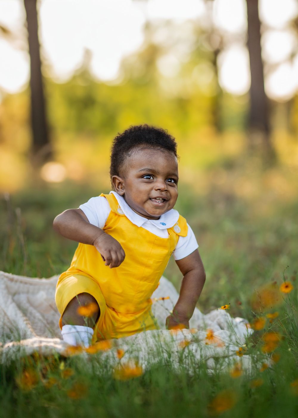 A child in a bright yellow dress sits in a field of wildflowers during golden hour.